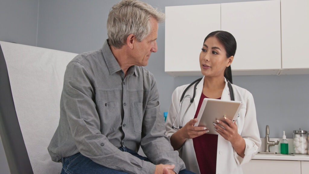 Primary Care Doctor Explaining Medical Issue To Senior Male Patient In Exam Room